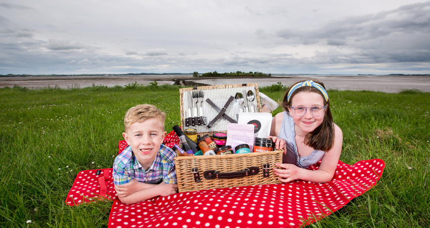 Two children pose with a picnic hamper on grass